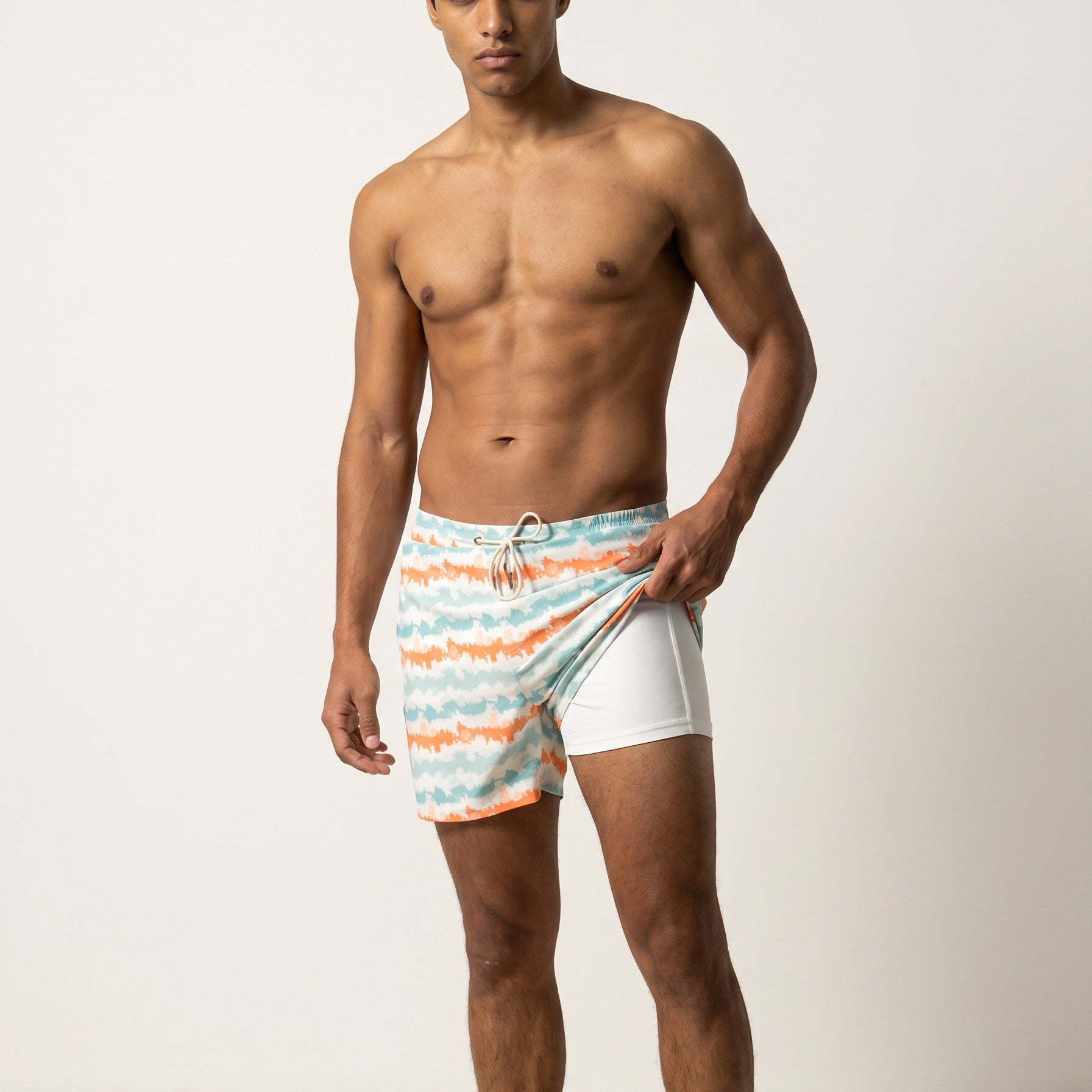 Man wearing coral and aqua striped Jack Rabbit Swims swim shorts, showing white inner lining
