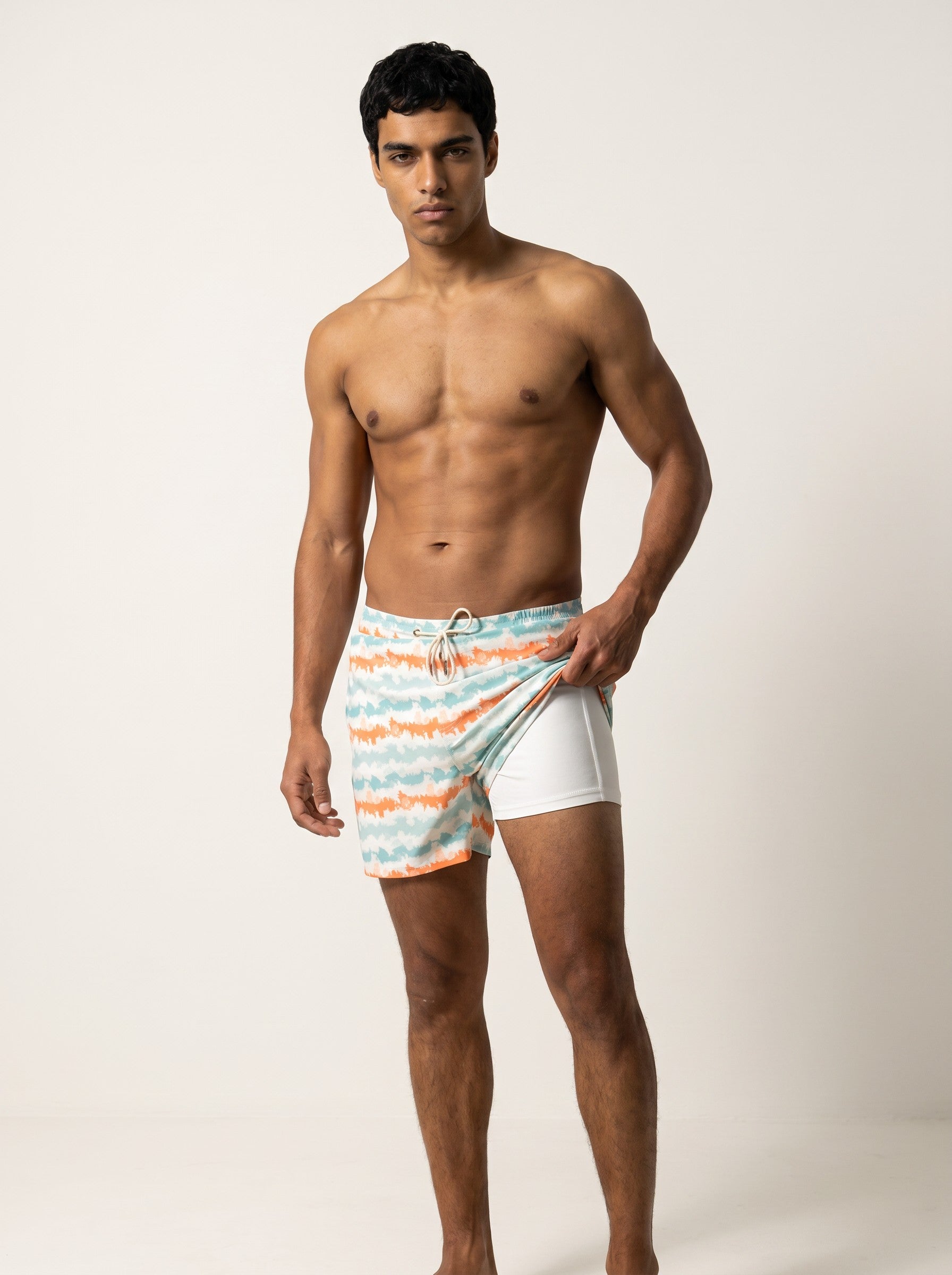 Man wearing coral and aqua striped Jack Rabbit Swims swim shorts, showing white inner lining